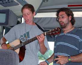 photo of Sarah Schneider and James Carrano leading pilgrims in song on bus