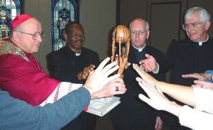 photo of Bishop Bullock praying as he and others outstretch hands toward statue