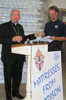photo of Bishop Morlino handing Ralph Middlecamp of the Society of St. Vincent de Paul a donation for a mattress set