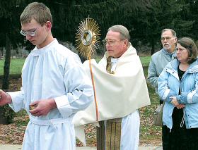 photo of Fr. Gerald Langsch bearing the monstrance and Blessed Sacrament during a Eucharistic procession, as adorers follow